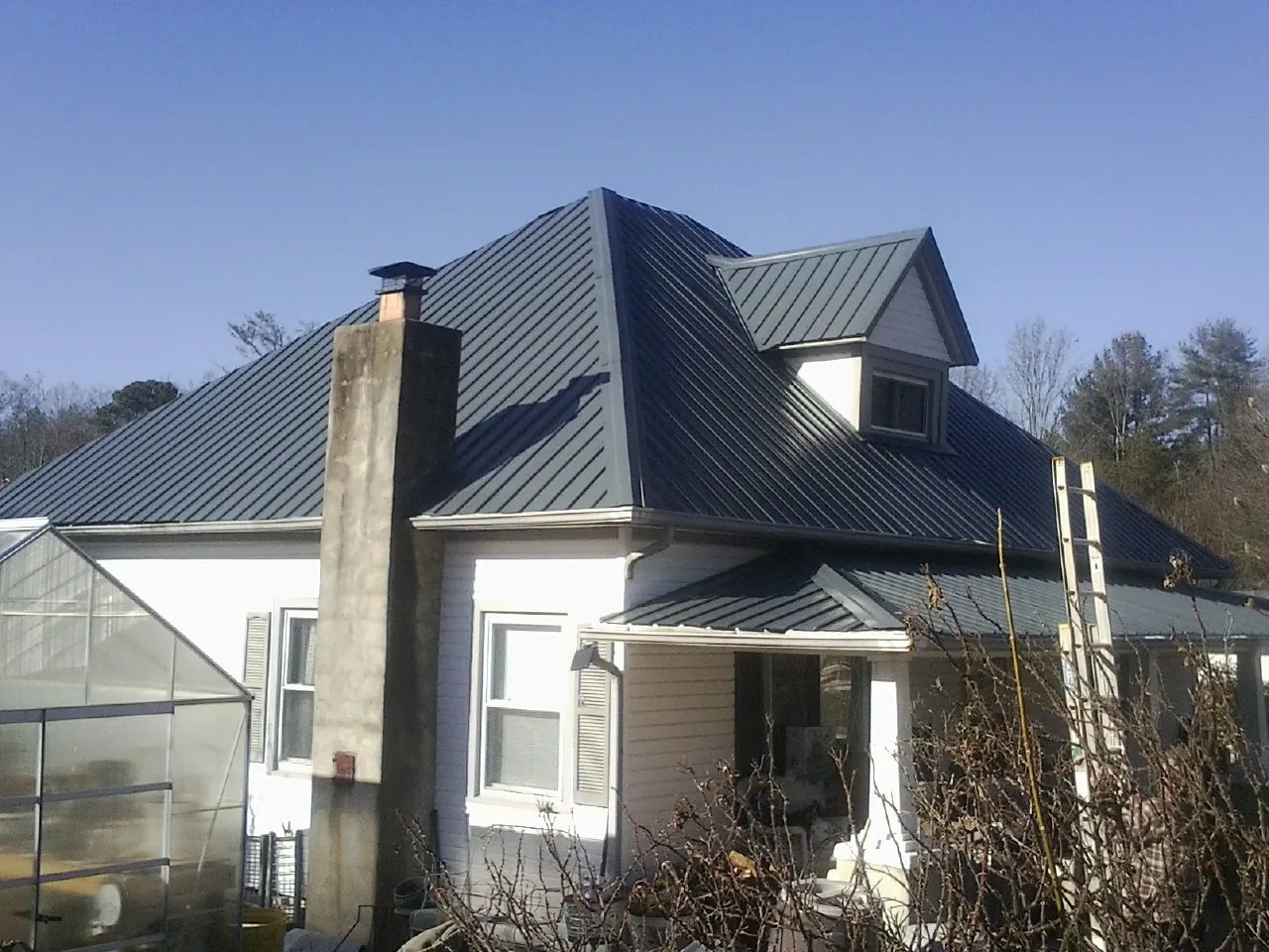 Dark blue standing seam metal roof on a white farmhouse with dormer in Lewistown