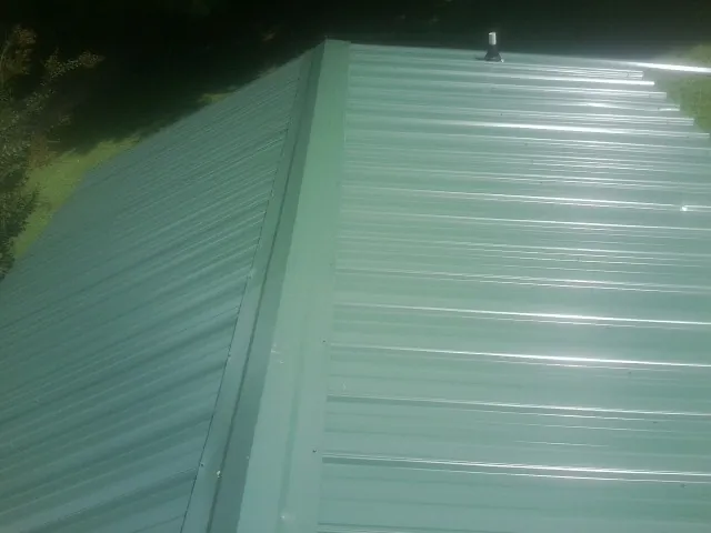 New green metal panels meeting at the ridge of a roof — Flat Roof Repair work by our crew in Lewistown